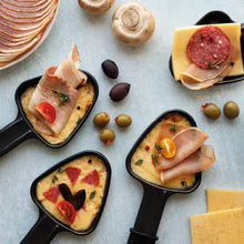 Raclette-Pfännchen mit Schinken, Käse und Oliven neben Wurstaufschnitt