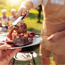 Mann grillt Fleischspieße und Steaks am Kugelgrill im Garten