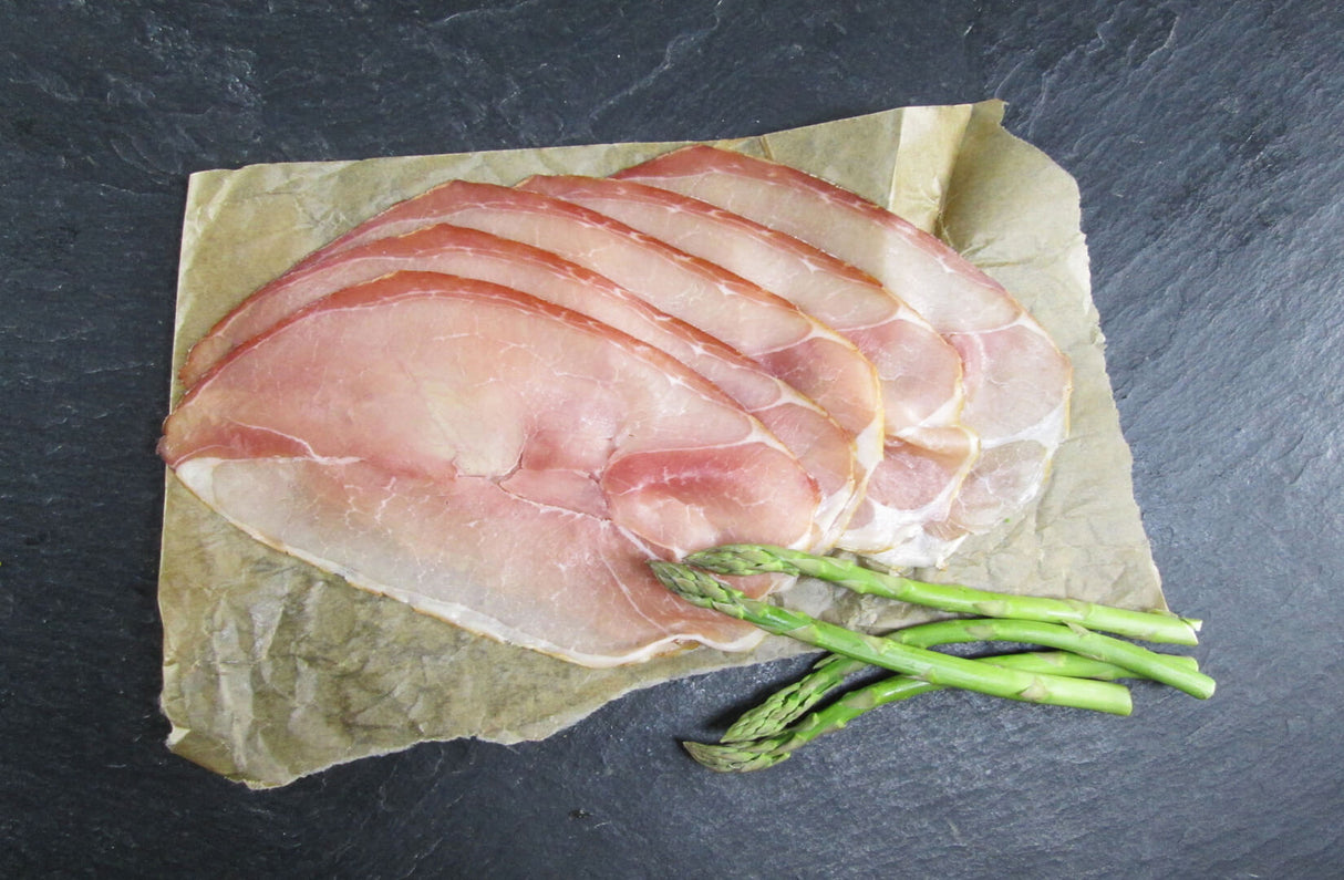 Rohschneider in Scheiben geschnitten angerichtet auf Backpapier mit grünem Spargel auf Schieferhintergrund