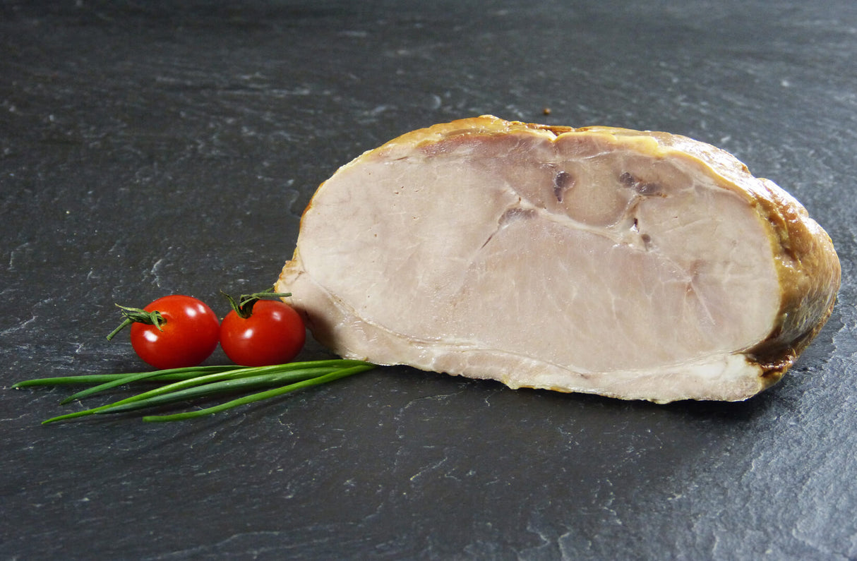 Schweinegrillbraten Aufschnitt am Stück mit Schnittlauch und Tomaten auf Schieferhintergrund