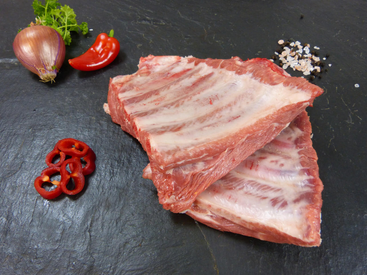 Spareribs von der Brustspitze roh mit Paprika und Zwiebeln sowie Gewürzen auf Schiefer