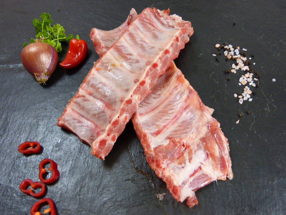 Kotelett Rippchen Spareribs frisch am Stück mit Paprika und Zwiebeln mit Pfferkörnern und Petersilie auf Schieferhintergrund