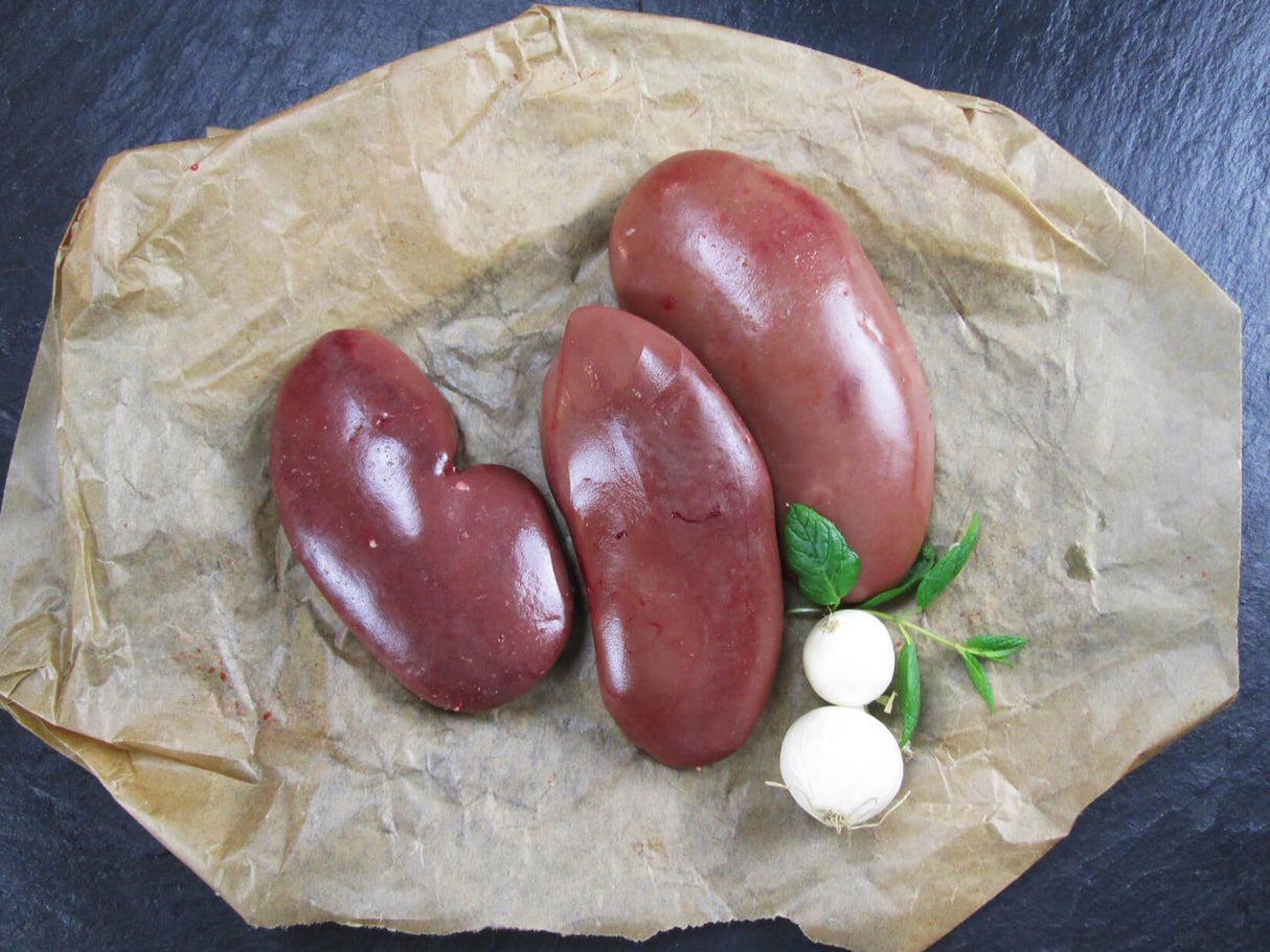 Drei Schweinenieren angerichtet Backpapier auf Schieferhintergrund