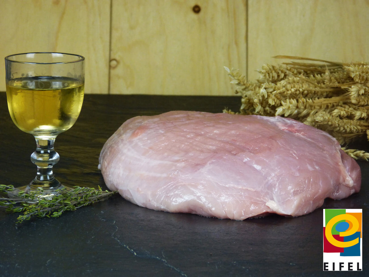 Schweineoberschale vom EIFEL Schwein angerichtet mit Thymian Weizen und einem Weinglas auf einem Schieferholzhintergrund im Vordergrund recht das Regionalmarke EIFEL Logo