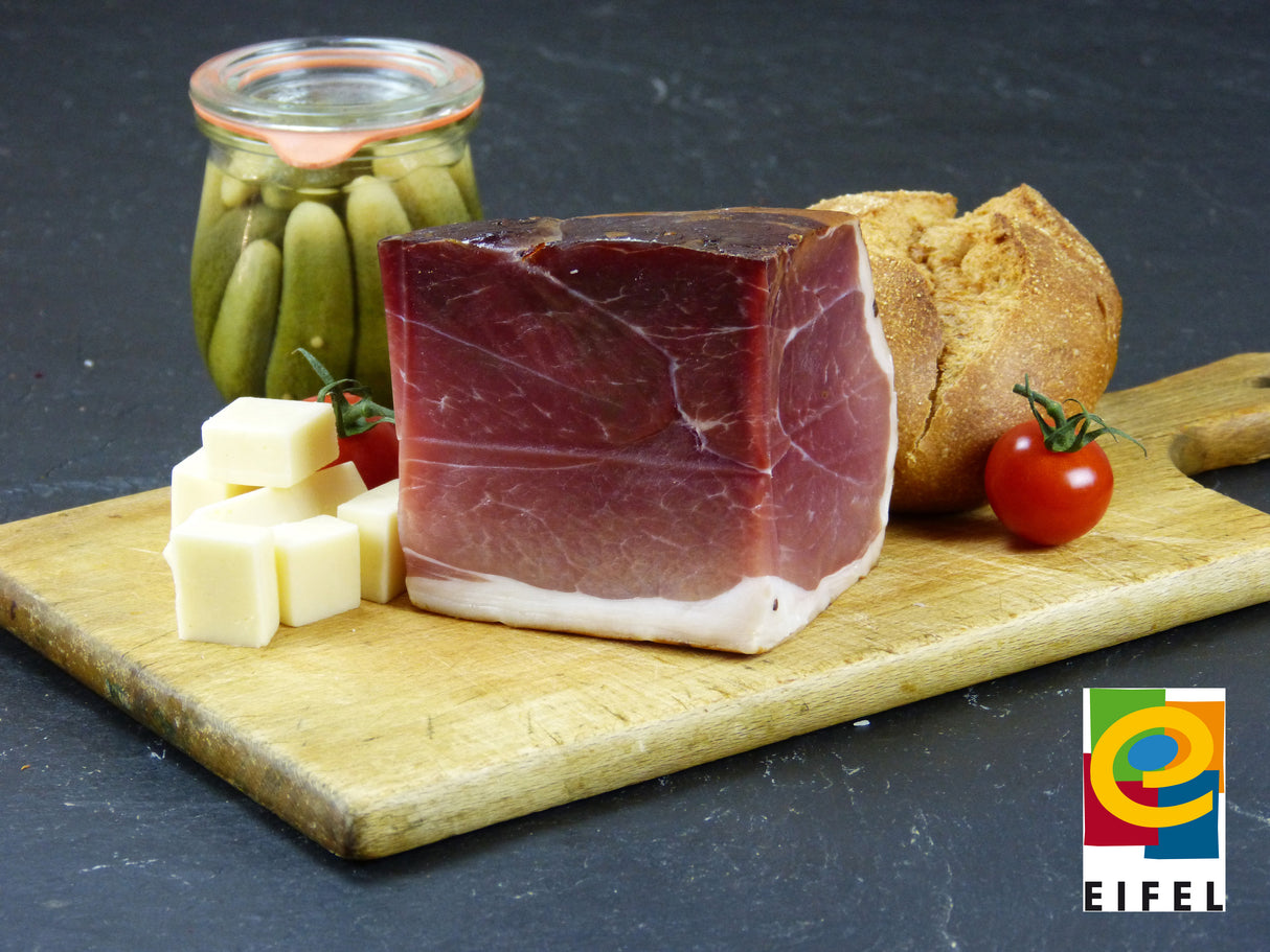 Bauernschinkenstück vom EIFEL Schwein mit Essigguken und Käsewürfeln und Brötchen auf Schieferhintergrund