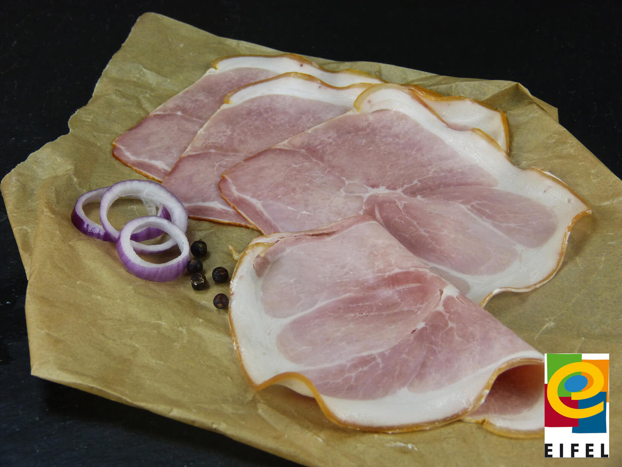 Metzgerschinken vom EIFEL Schwein angerichtet mit Wachholderbeeren und roten Zwiebelringen auf Backpapier mit Schieferhintergurnd und einem EIFEL Regionalmarke Logo unten rechts in der Ecke