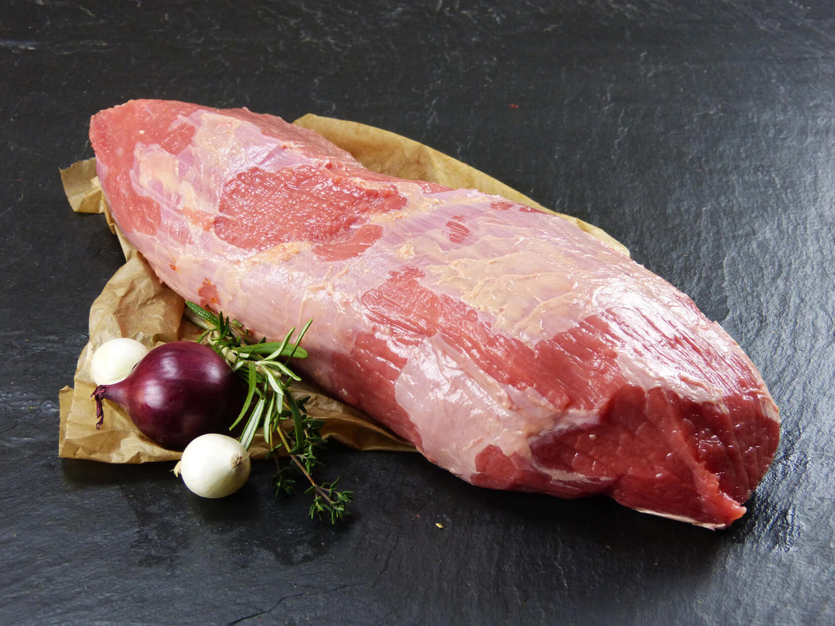 Semerrolle vom EIFEL Rind angerichtet mit Silberzwiebeln Thymian und einer roten Zwiebel auf Backpapier mit Schieferhintergrund