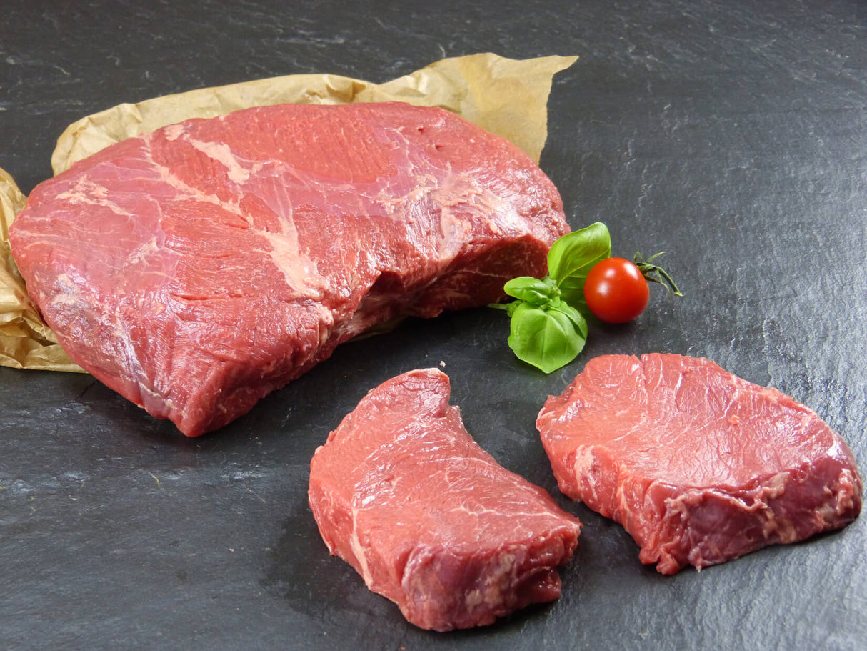 Argentinische Rindersteakhüfte mit einem Großen stück und zwei kleineren angerichtet mit Basilikum einer Tomate auf Backpapier mit Schieferhintergrund