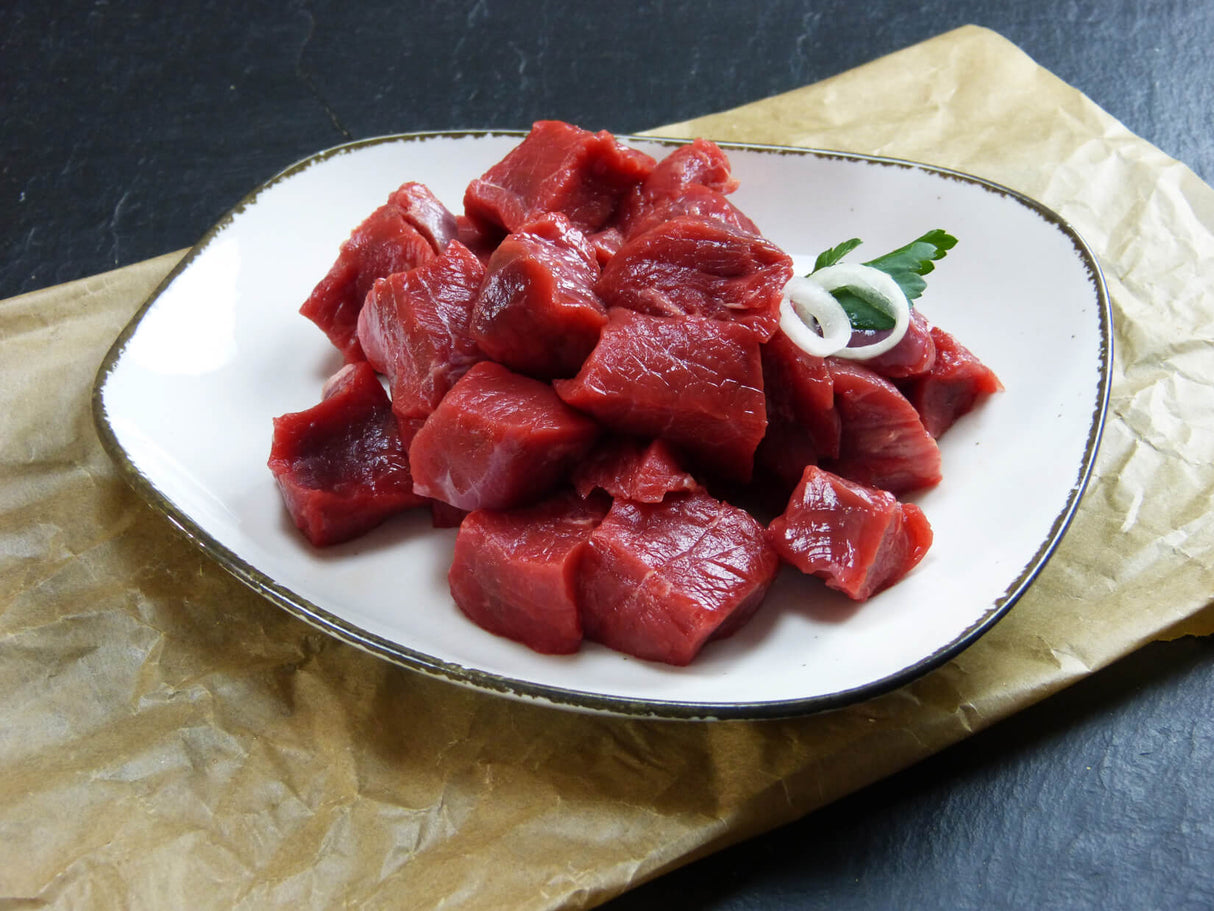 Rinder Gulasch vom Bugstück vom EIFEL Rind angerichtet mit Zwiebelringen in einer Schüssel auf Backpapier mit Schieferhintergrund