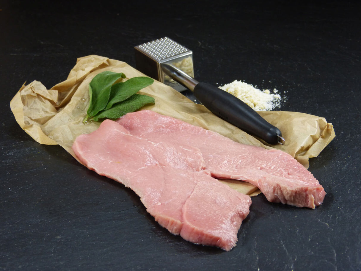 Kalb Oberschalenschnitzel präsentiert auf Backpapier mit einem Fleischklopfer und Minze auf schwarzer Schieferplatte