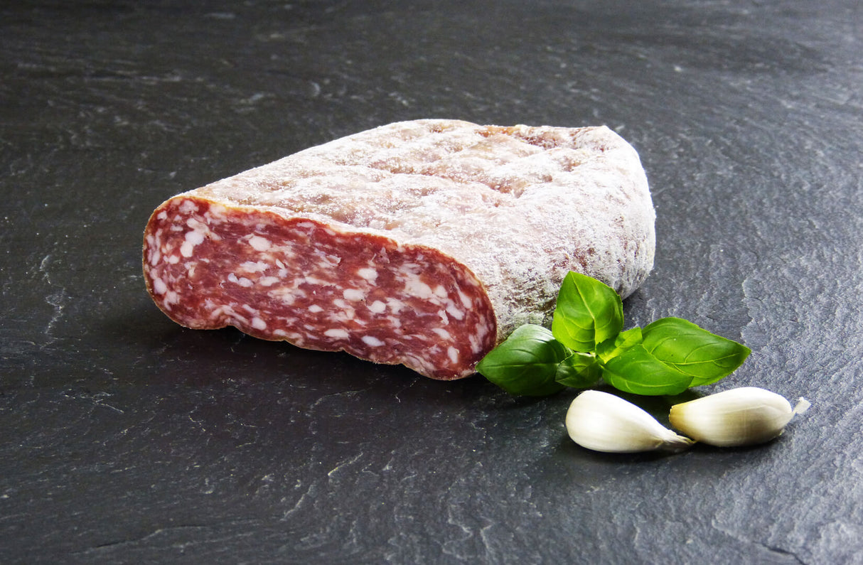 Salami Spianata Romana am Stück angerichtet mit Knoblauch und Basilikum auf Schieferhintergrund