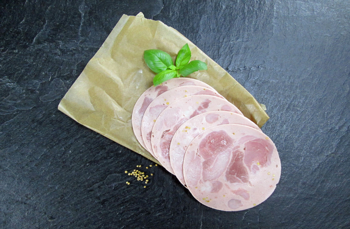 Bierschinken geschnitten mit Senfkörner und Basilikumblätter auf Backpaprier auf Schieferhintergrund