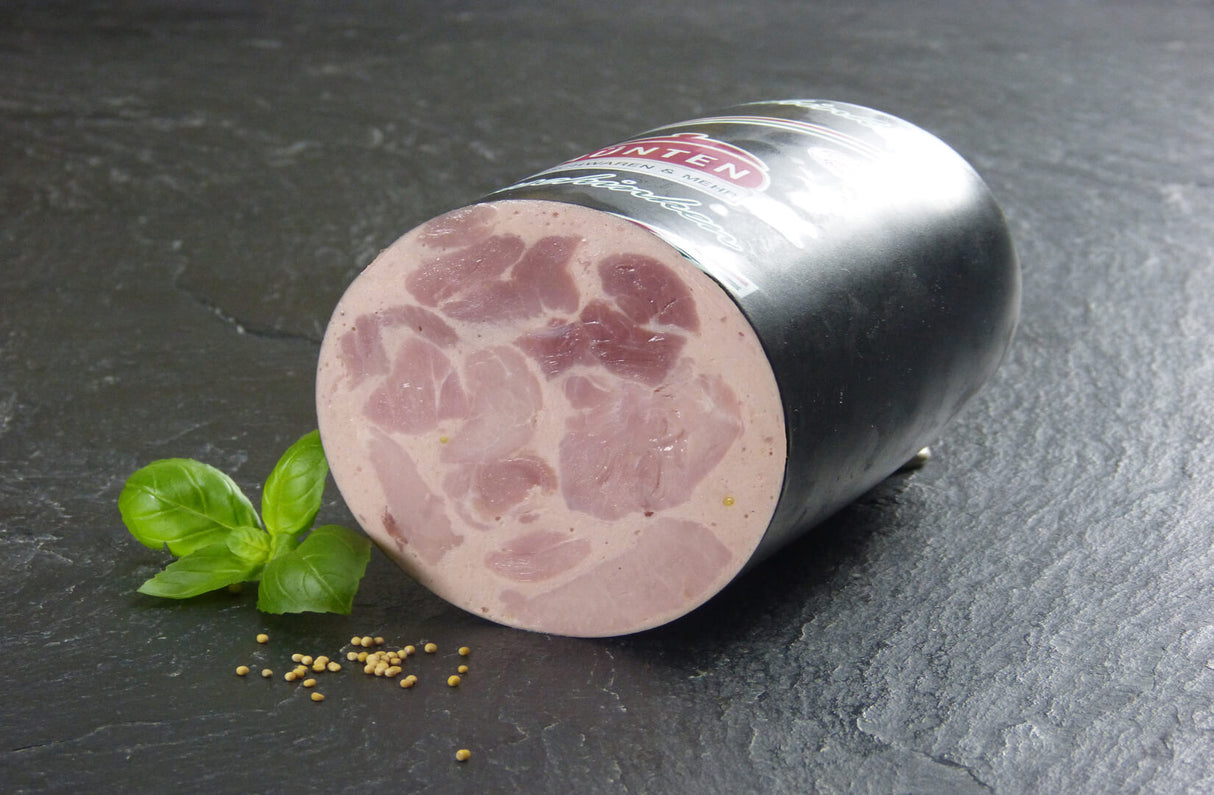 Bierschinken halbes Stück mit Senfkörnern und Basilikumblättern auf Schieferhintergrund