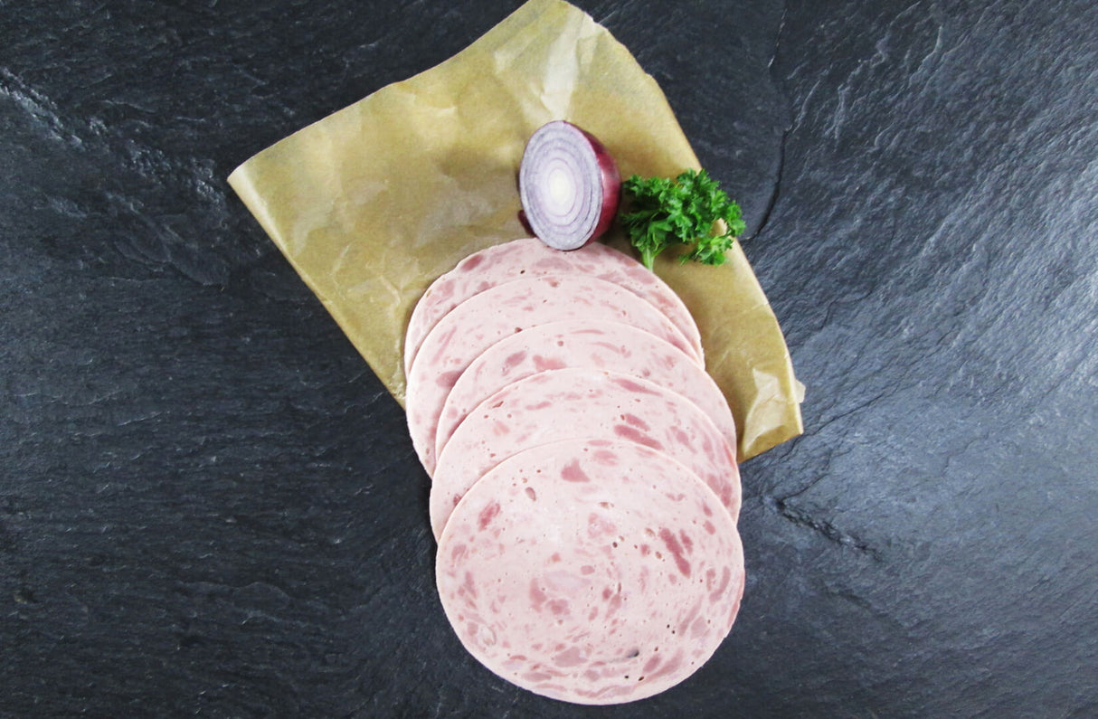 Fünf scheiben Jagdwurst angerichtet mit einer halben roten Zwiebel und Petersilie auf einem Backpapier mit Schieferhintergrund