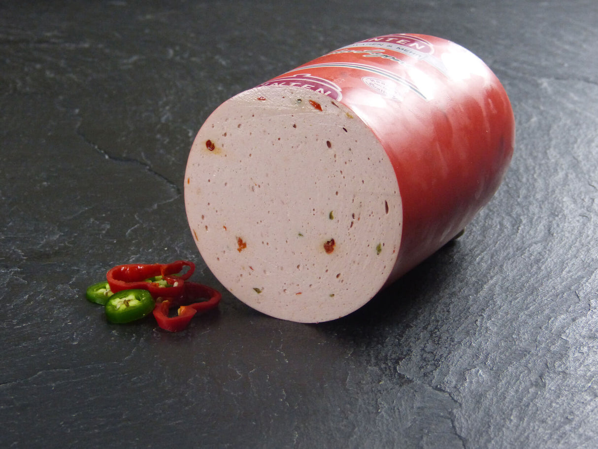 Eine halbe Paprikawurst angerichtet mit zwei scheiben einer roten Paprika und einer grünen auf Schieferhintergrund