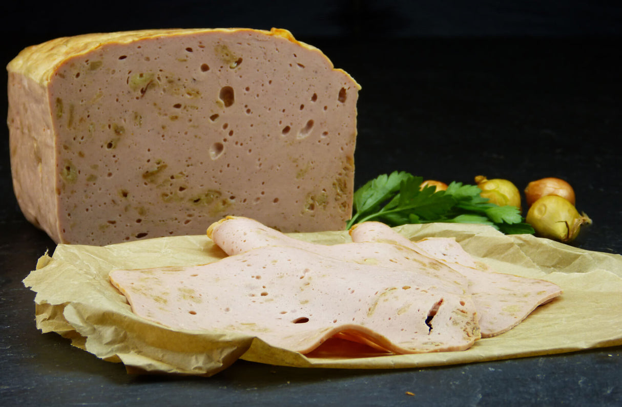 Ein halber Zwiebelfleischkäse gebacken und zwei Scheiben geschnitten vom EIFEL Schwein angerichtet mit Petersilie und vier kleinen Zwiebeln auf Backpapier mit Schieferhintergrund