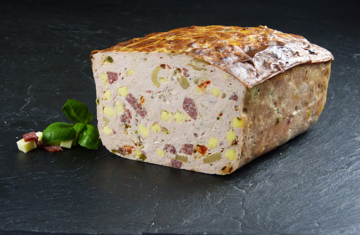 Ein halber Pizzafleischkäse gebacken vom EIFEL Schwein angerichtet mit Salamiwürfeln Käsewürfeln und Basilikum auf Schieferhintergrund