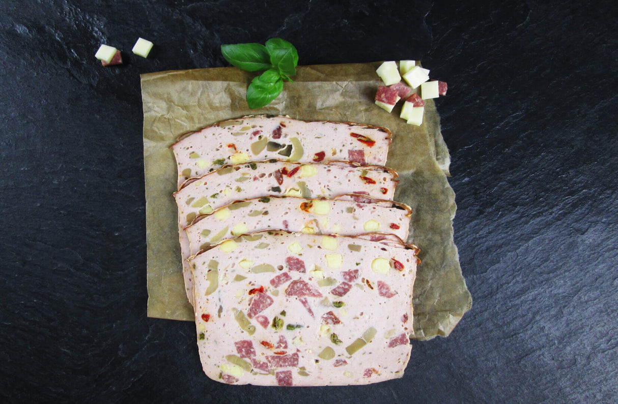 Vier scheiben Pizzafleischkäse gebacken vom EIFEL Schwein angerichtet mit Salamiwürfeln Käsewürfeln und Basilikum auf Backpapier mit Schieferhintergrund