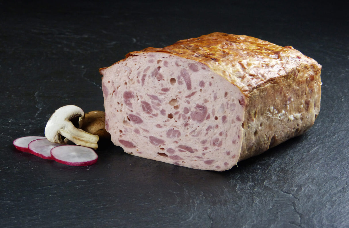 Ein halber Fleischkäse grob gebacken vom EIFEL Schwein angerichtet mit drei Scheiben eines Radieschens und ein halbierter Champignonpilz