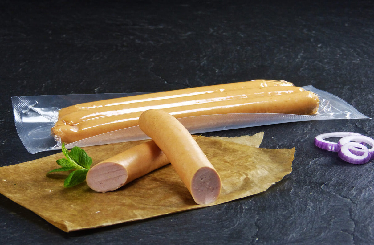 Drei Wiener Würstchen verpackt vom EIFEL Schwein und ein halbiertes Wienerwürschen angerichtet mit Minze und drei roten Zwiebelringen auf Backpapier mit Schieferhintergrund