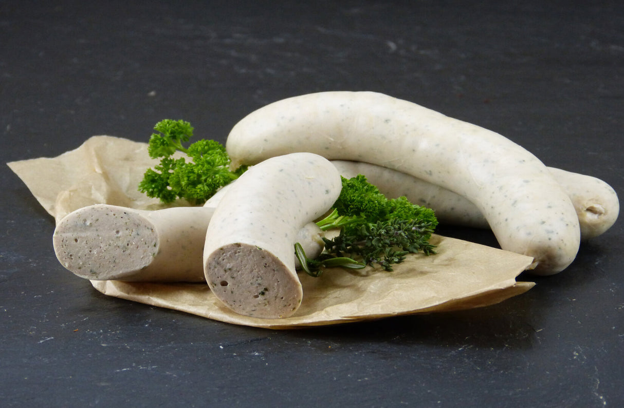 Zwei Jubiläumsbratwürste und einer halbierten Jubiläumsbratwurst angerichtet mit Petersilie auf Backpapier mit Schieferhintergrund