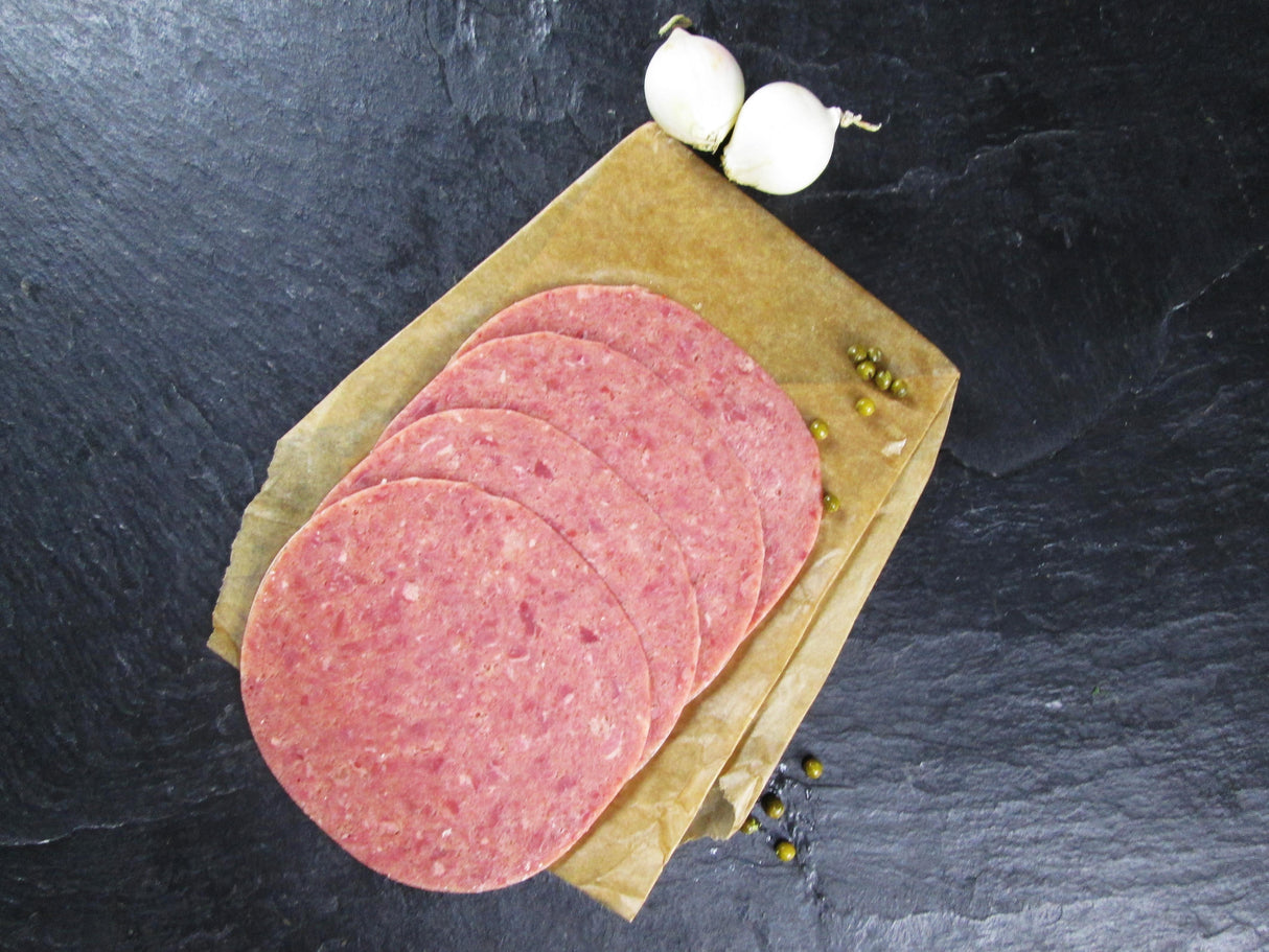 Vier scheiben Deutsches Cornedbeef angerichtet mit zwei kleinen Zwiebeln und ein paar Erbsen auf Backpapier mit Schieferhintergrund