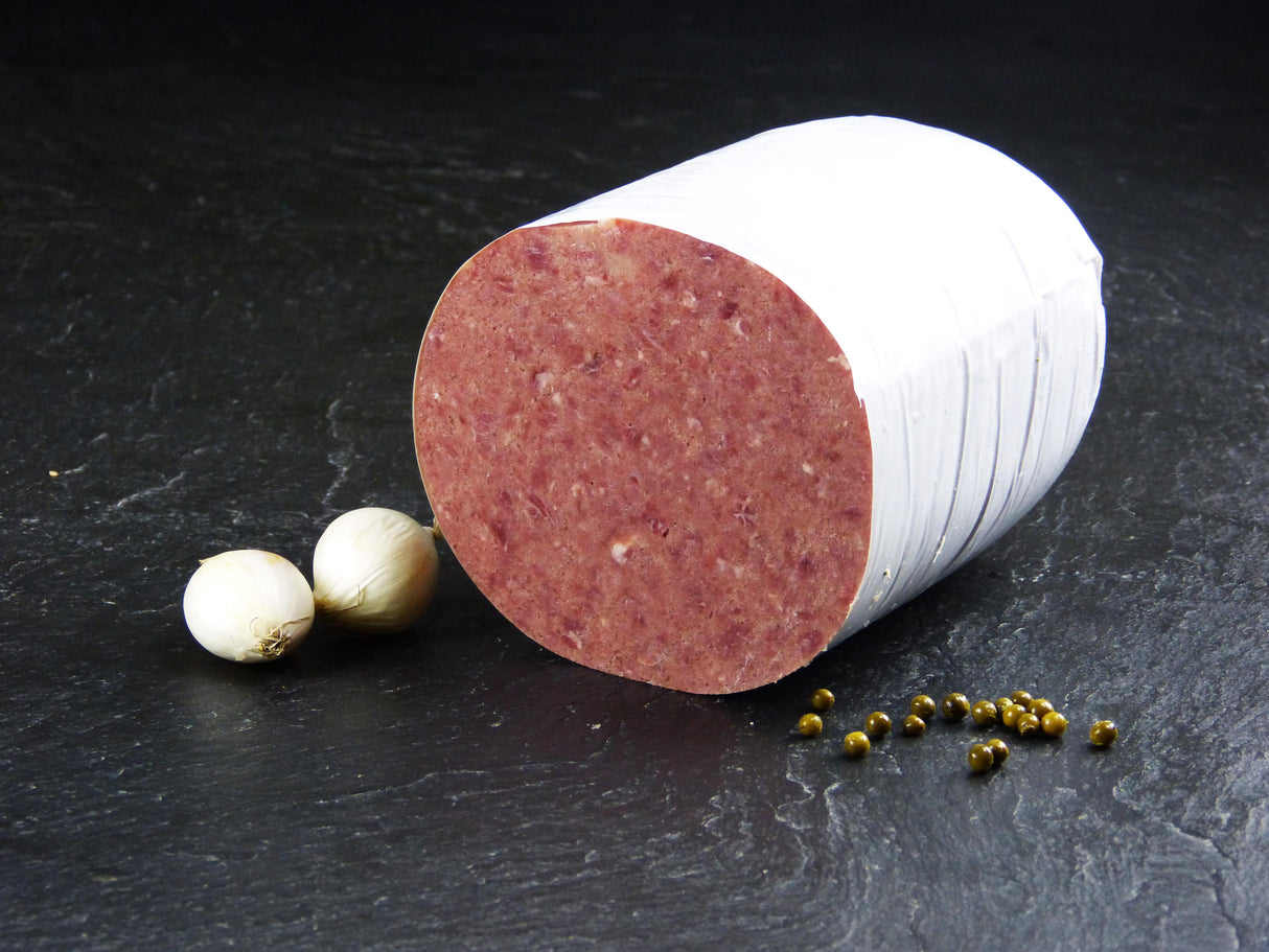 Ein hälfte vom Deutschen Cornedbeef angerichtet mit zwei kleinen Zwiebeln und paar Erbsen auf Schieferhintergrund