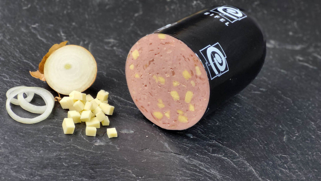 Anschnitt vom Lyoner Cheese und Onions vom EIFEL Schwein angerichtet mit einer halben zwiebel Käsewürfeln und Zwiebelringen auf Schieferhintergrund