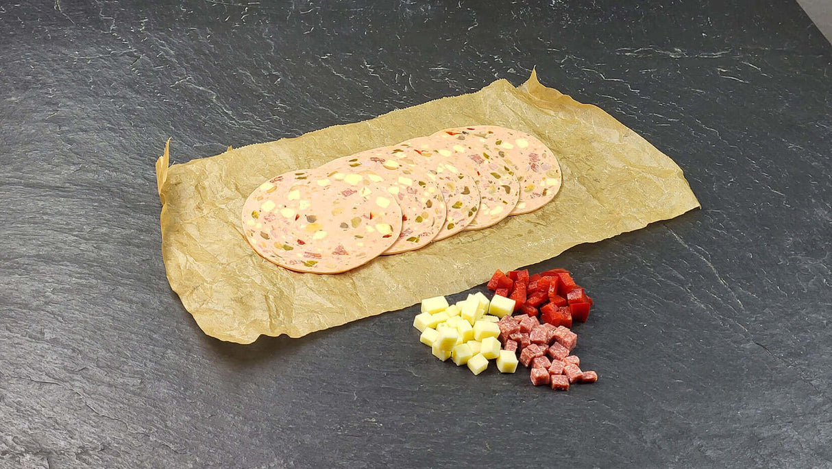 Fünf scheiben Pizza Lyoner vom EIFEL Schwein angerichtet mit Käsewürfeln Salamiwürfeln und Paprikawürfeln auf Backpapier mit Schieferhintergrund