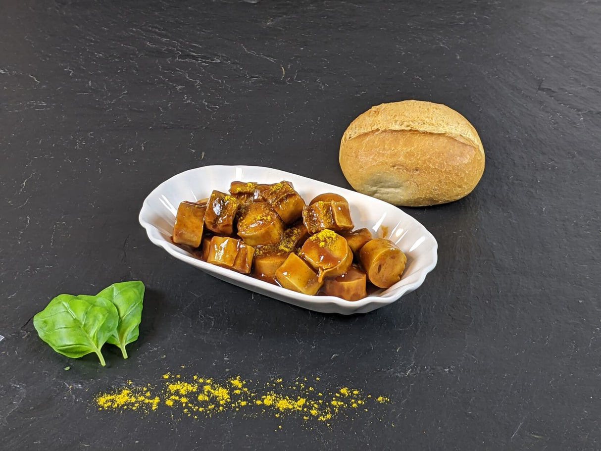 Currywurst vom EIFEL Schwein angerichtet im Teller mit einem Brötchen Basilikum und Currypulver mit Schieferhintergrund