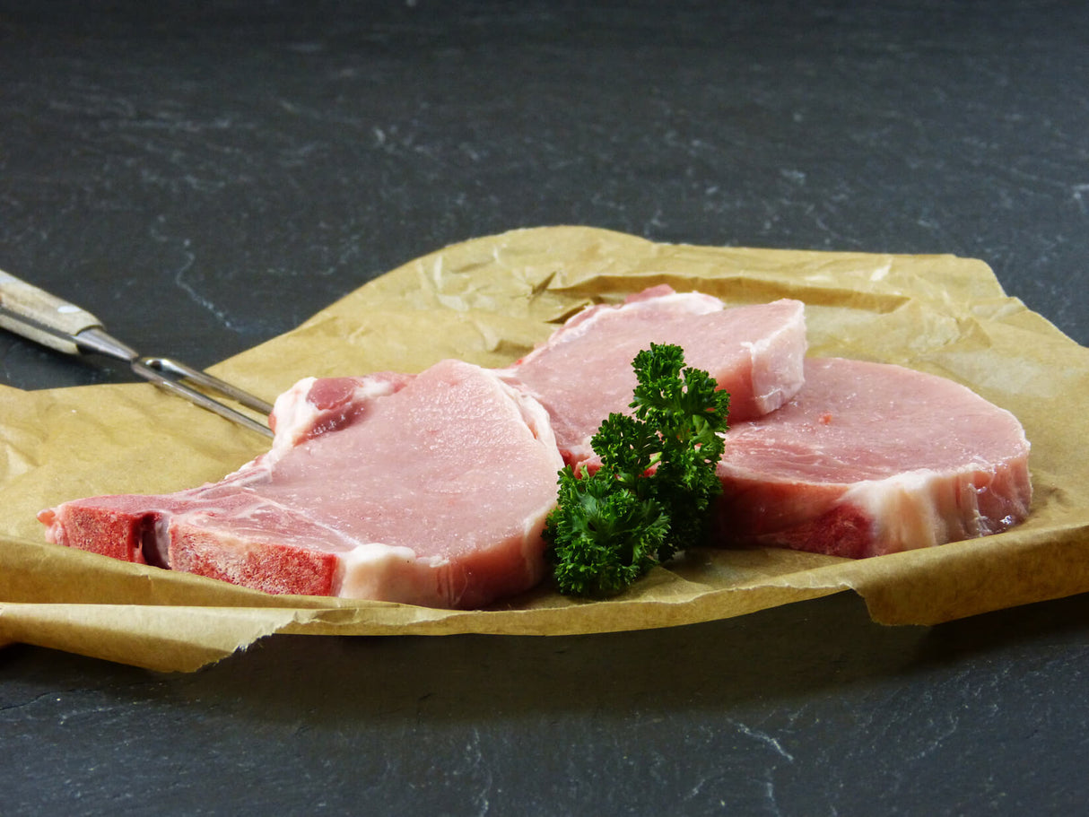 Drei Stielkotelett angerichtet mit Petersilie und einer Fleischgabel auf Backpapier mit Schieferhintergrund