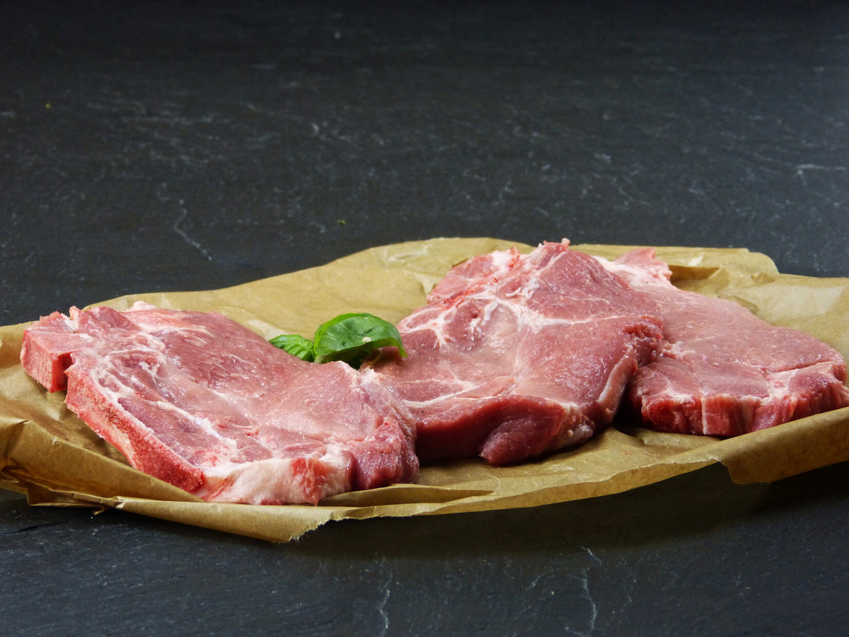 Drei Kammkotelett angerichtet mit Basilikum auf Backpapier mit Schieferhintergrund