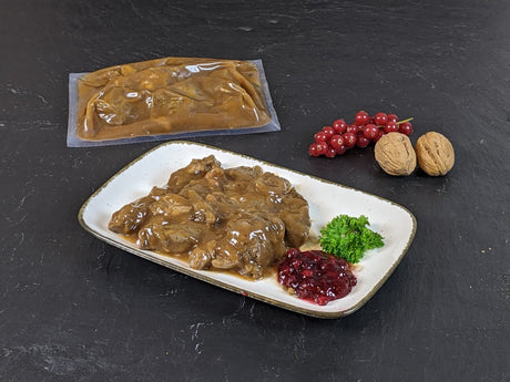 Hirschgulasch in Preiselbeer Rotweinsauce im Kochbeutel und gegart auf Teller mit Preiselbeeren auf Schieferhintergrund
