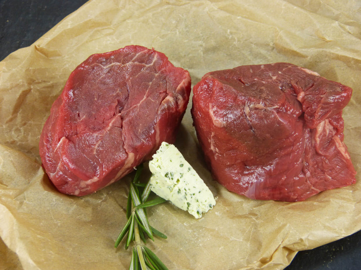 Zwei Argentinische Filetsteaks angerichtet mit Kräuterbutter un Thymian auf Backpapier mit Schieferhintergrund