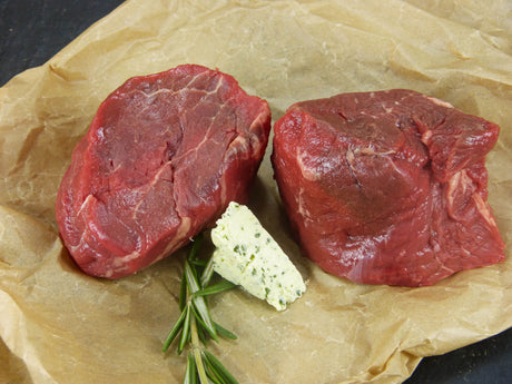 Zwei Argentinische Filetsteaks angerichtet mit Kräuterbutter un Thymian auf Backpapier mit Schieferhintergrund