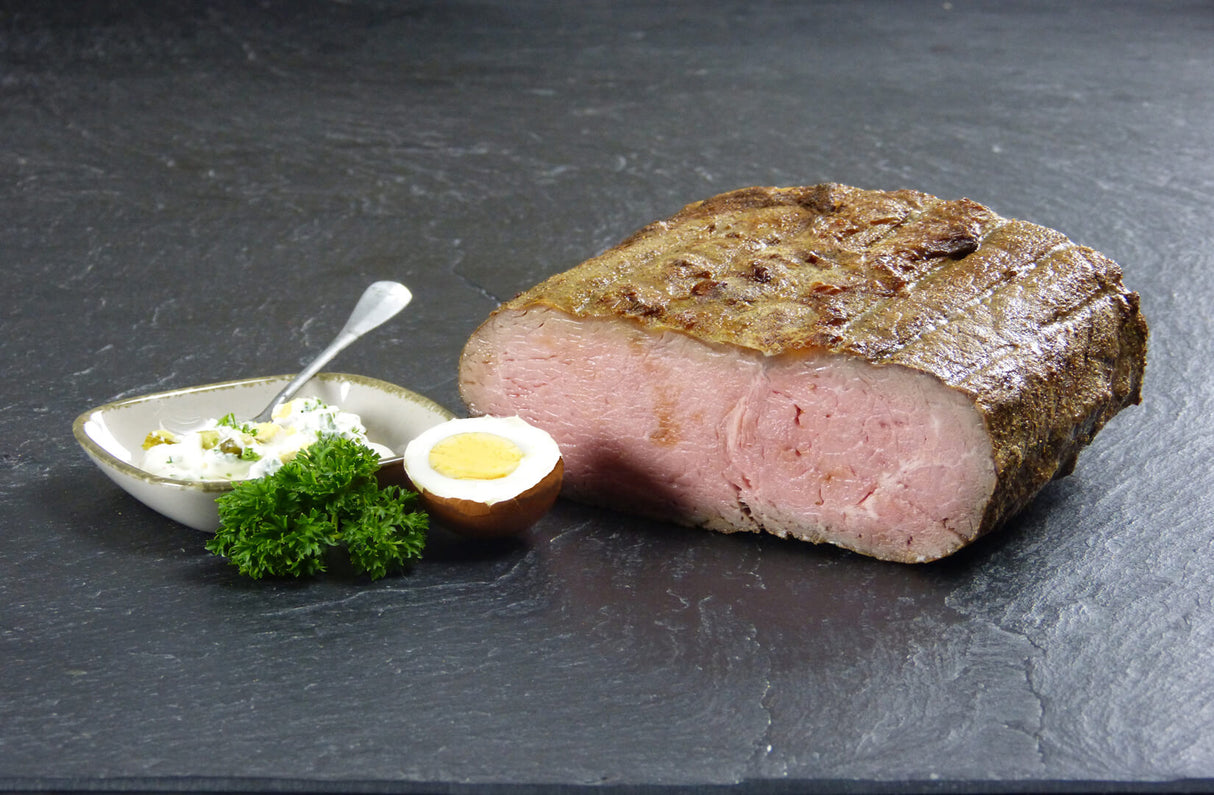 Roastbeefbraten am Stück und in Scheiben geschnitten mit gekochten Ei und Remouladensauce auf Schieferhintergrund