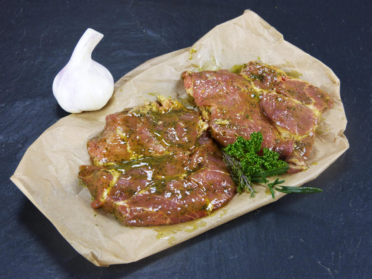 Zwei Schweinenackensteaks Kräuter Knoblauch angerichtet mit einer Knoblauchknolle Rosmarin und Thymian auf Backpapier mit Schiefehintergrund