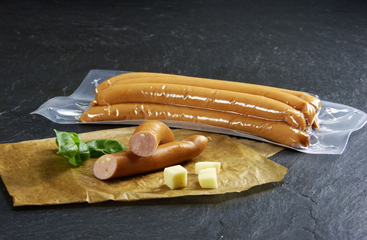 Käsewiener vom EIFEL Schwein verpackt und eine halbierte Käsewiener angerichtet mit Basilikum und Käsewürfeln auf Backpapier mit Schieferhintergrund