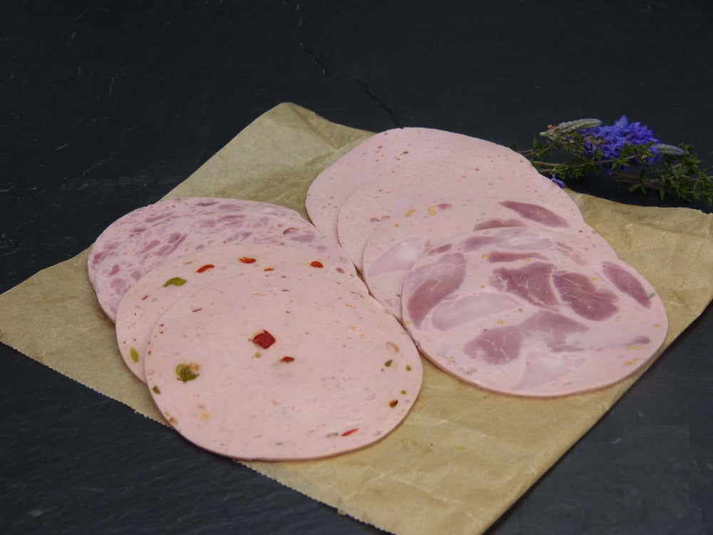 Zwei scheiben Bierschinken Jagdwurst Fleischwurst und Paprikawurst angerichtet mit Rosmarin auf einem Backpapier mit Schieferhintergrund