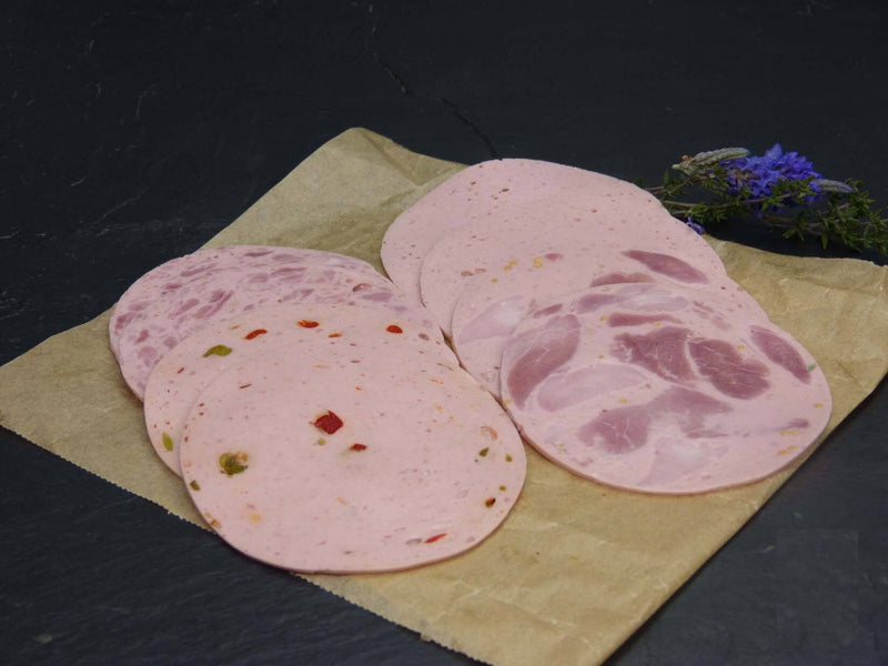 Zwei scheiben Bierschinken Jagdwurst Fleischwurst und Paprikawurst angerichtet mit Rosmarin auf einem Backpapier mit Schieferhintergrund