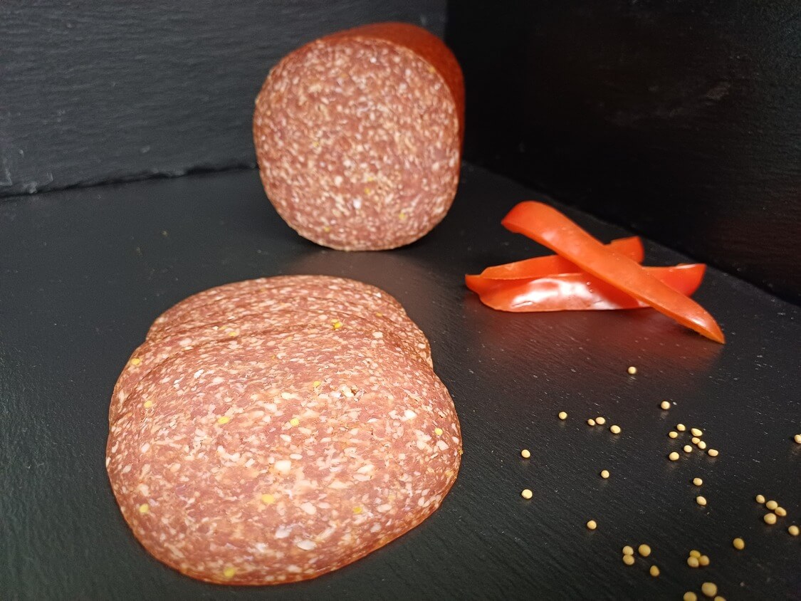 Bauernsalami Ungarische Art am Stück und geschnitten mit Dekoration Senfkörnern und Paprika