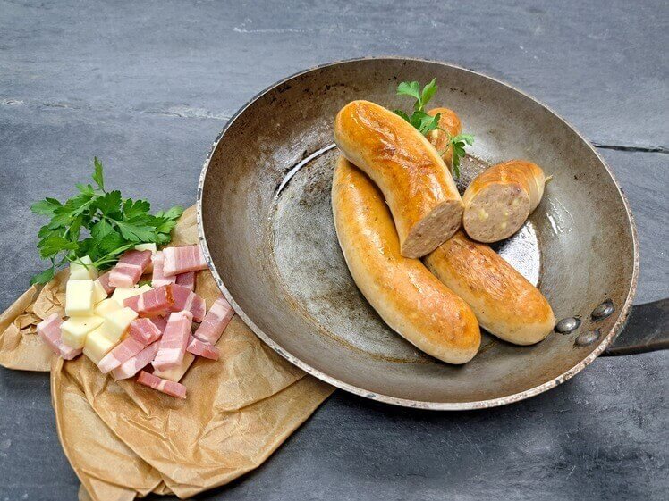 Bratwurst Bacon Cheese gebraten in der Pfanne mit Käsewürfeln und Baconwürfeln aus Schieferhintergund