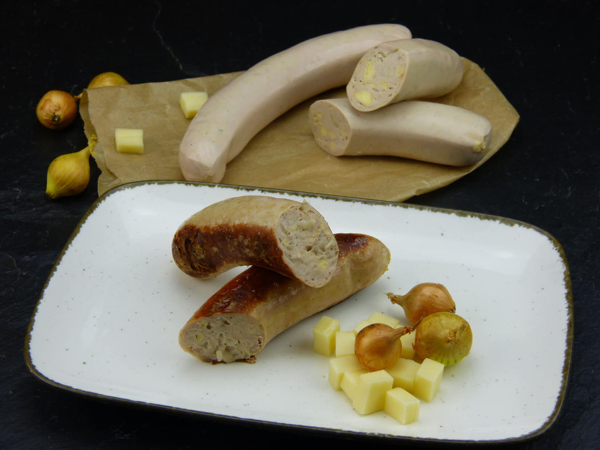Bratwurst Cheese und Onion gebraten vom EIFEL Schwein auf Teller dekoriert mit Käsewürfeln und Zwiebeln im Hintergrund eine rohe Bratwurst Cheese und Onion mit Käsewürfeln und Zwiebeln auf Backpapier und Schieferhintergrund