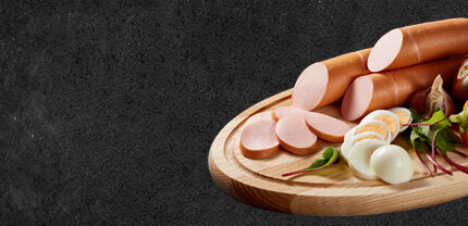 Fleischwurst im Ring auf einem Holzbrett mit Eiern auf Schieferhintergrund