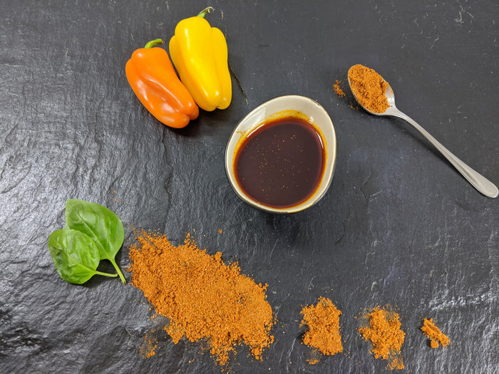 Paprika Marinade angerichtet mit Paprika Pulver Basilikum einer gelben Paprika und einer orangenen Paprika