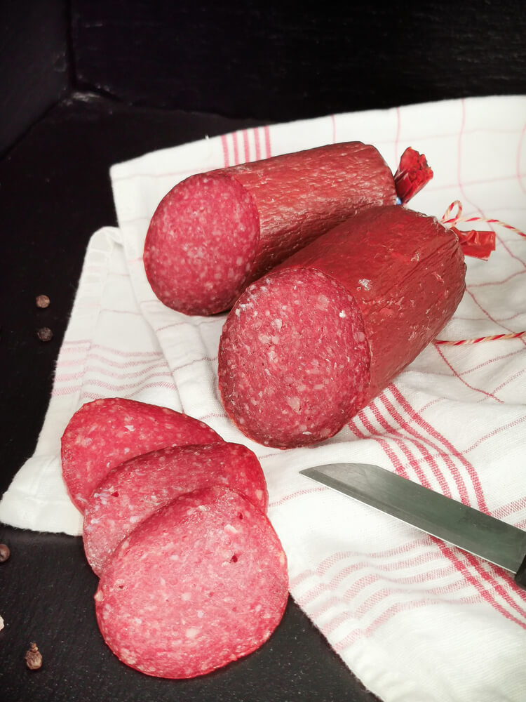 Angeschnittene Rindersalami am Stück, dekoriert auf Küchentuch mit Messer