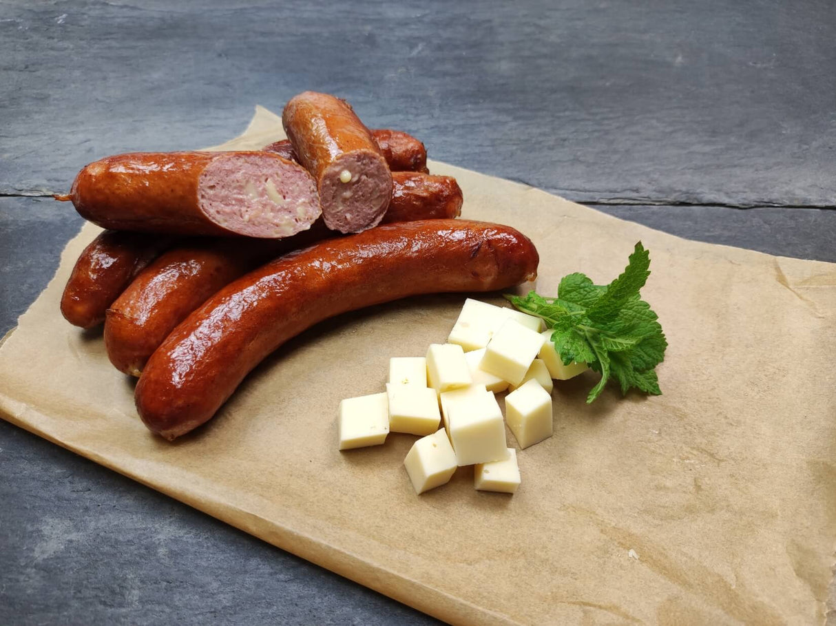 Rindswurst mit Käse vom EIFEL Rind gebraten mit Käsewürfeln und Minze auf Backpapier und Schieferhintergrund
