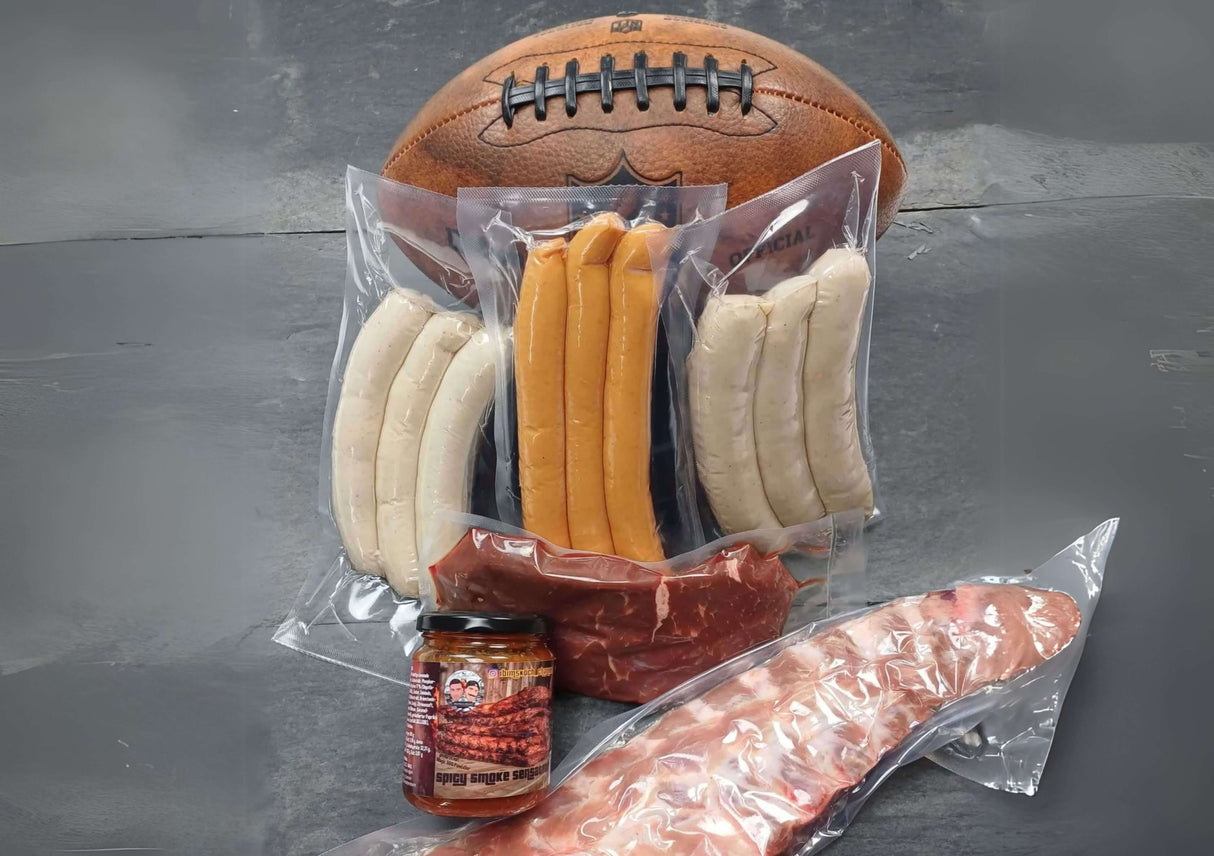 Super Bowl Box Spareribs von der Brustspitze Spicy smoke BBQ Sauce argentinisches Hüftsteak 3er Pack Wiener Würstchen 3er Pack Bratwurst und 3er Pack Käsebratwurst dekoriert mit fottball auf Schieferplatte