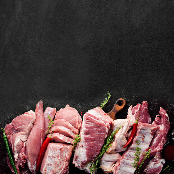 Rohes Fleisch angerichtet auf schwarem Hintergrund dekoriert mit Rosmarin und Peperoni