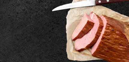 Lachskasseler angerichtet auf Backpapier mit Messer auf schwarzem Hintergrund